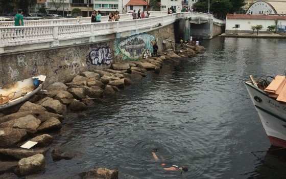 Homem mergulha no mar da Urca, enquanto outros observam, em busca do dinheiro