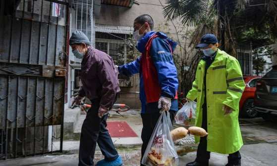 Dois voluntários acompanham um idoso em Wuhan, na China Foto: AFP