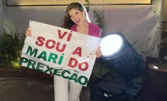 Mari com cartaz em frente a festa
