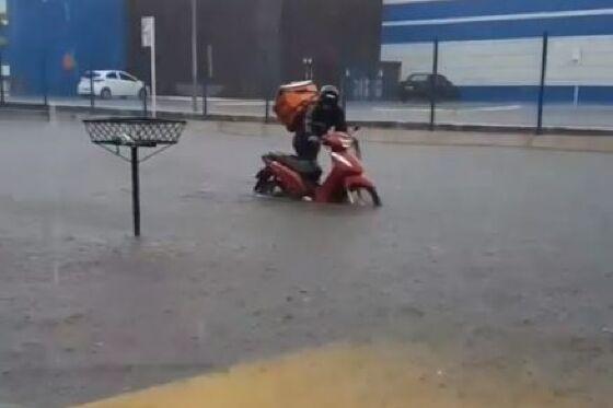 Entregador empurra moto em pista alagada