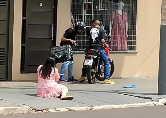 Mulher caída no chão e bandidos roubando a moto.