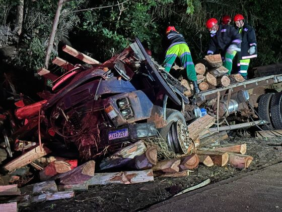Com o impacto da batida, a carga de madeira caiu sobre a cabine do veículo