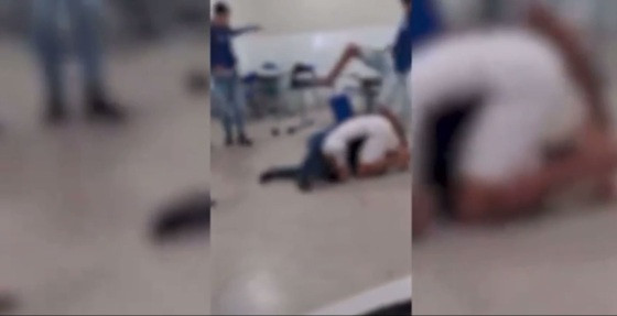As imagens mostram que um garoto de camisa branca imobiliza um colega uniformizado, fazendo ele cair no chão.