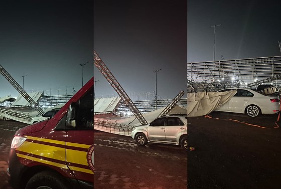 Na foto, é possível ver parte da estrutura tombada, além de um pano branco, que deve ser uma lona, caído sobre dois carros estacionados ao lado