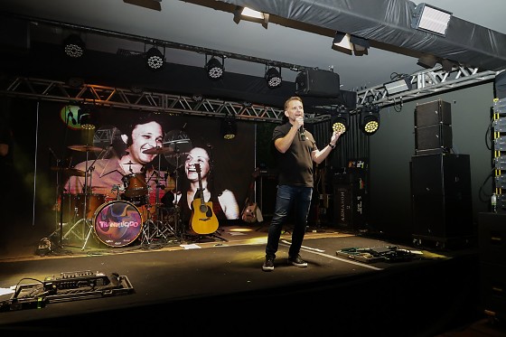 Foto de Stephany Siqueira (Genius Publicidade), com Brasa ao centro e imagem dos fundadores Luiz Gonzaga Rodrigues e Neusa Lula Rodrigues gerada por IA ao fundo