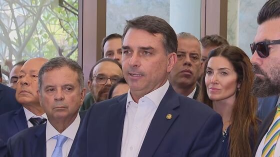 Flávio Bolsonaro durante evento de campanha, cercado por apoiadores e bandeiras do PL.