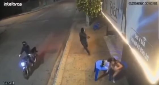 Câmera de segurança registrou o momento em que o atirador desceu da motocicleta e efetuou disparos contra a mulher em frente ao bar.